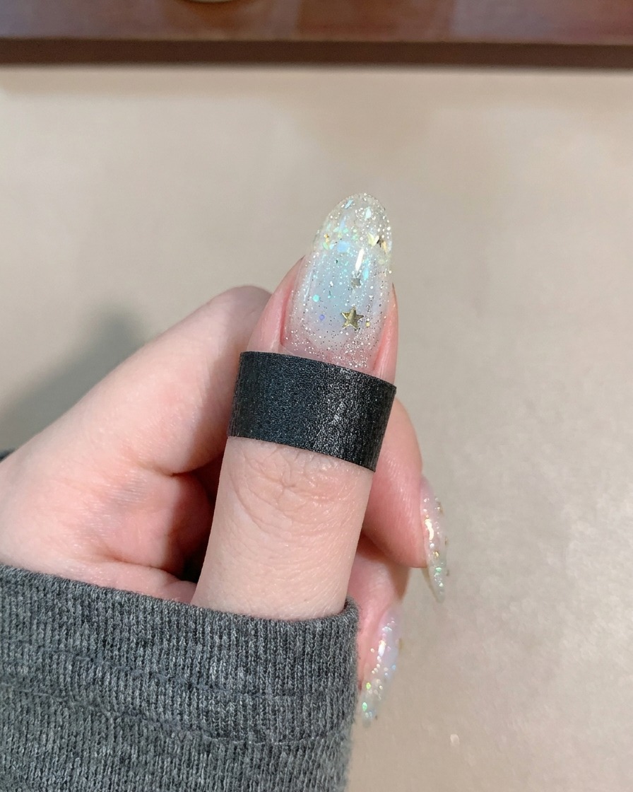 Un pincel aplicando un top coat transparente y brillante sobre una uña con estrellas y líneas.