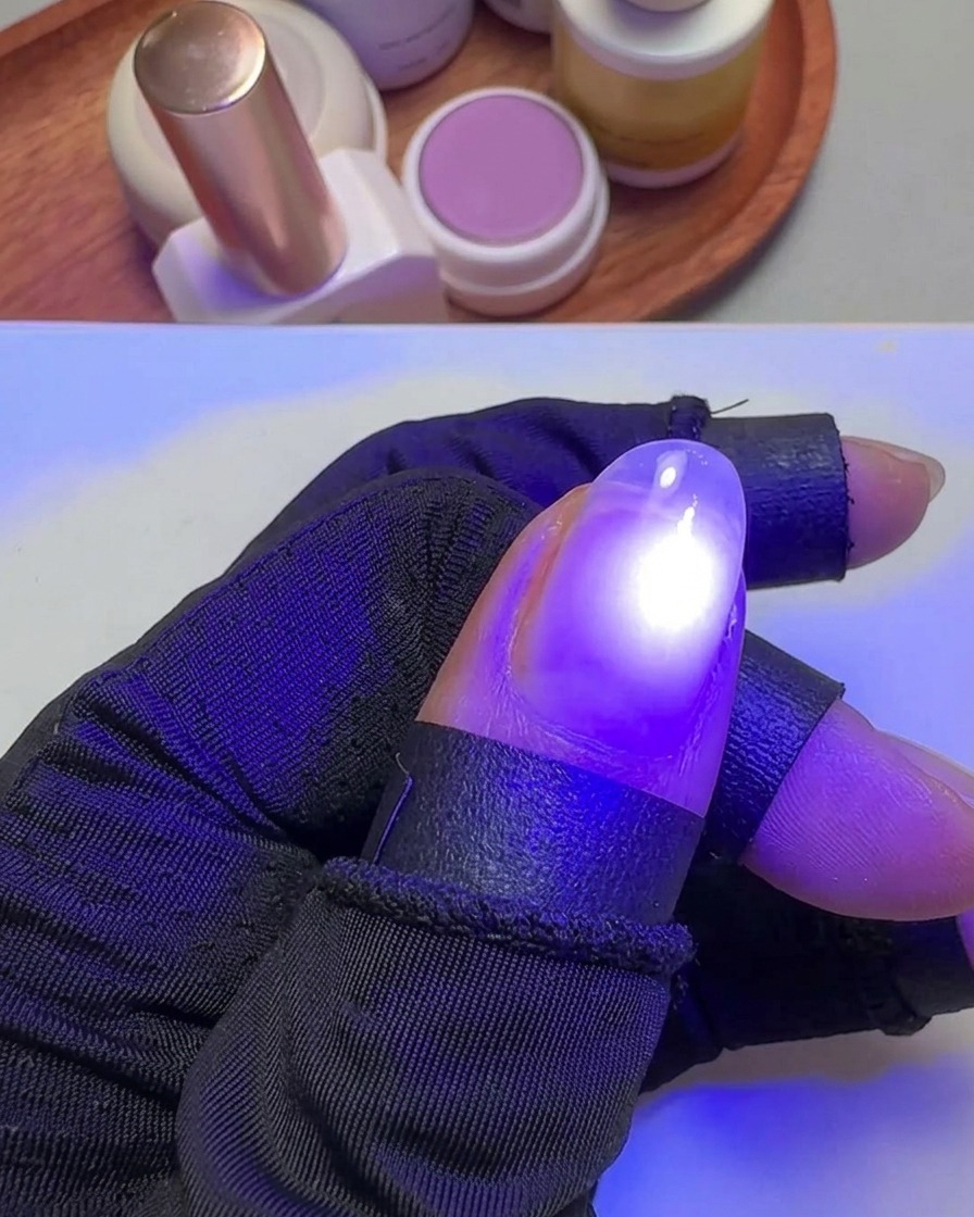 Una mano sosteniendo un pulgar bajo una pequeña lámpara UV violeta para curar el esmalte.