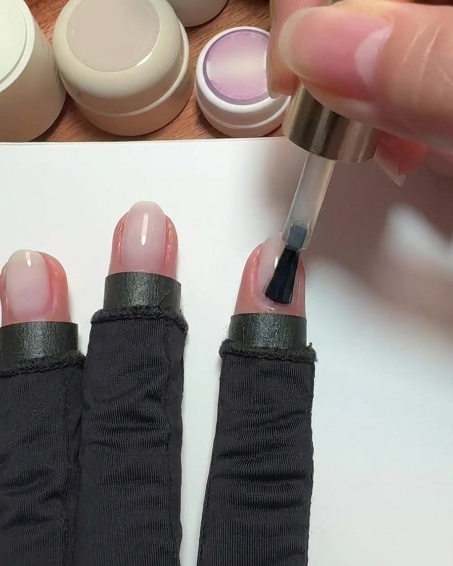 Un pincel aplicando esmalte de gel rosa nude sobre la uña de un dedo índice.