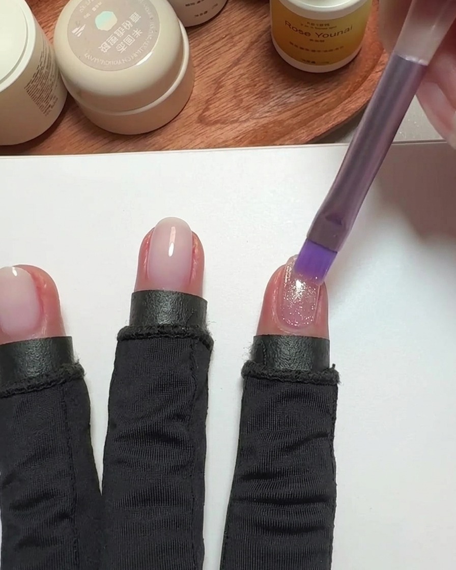 Un pincel aplicando esmalte cat-eye rosa sobre una uña.