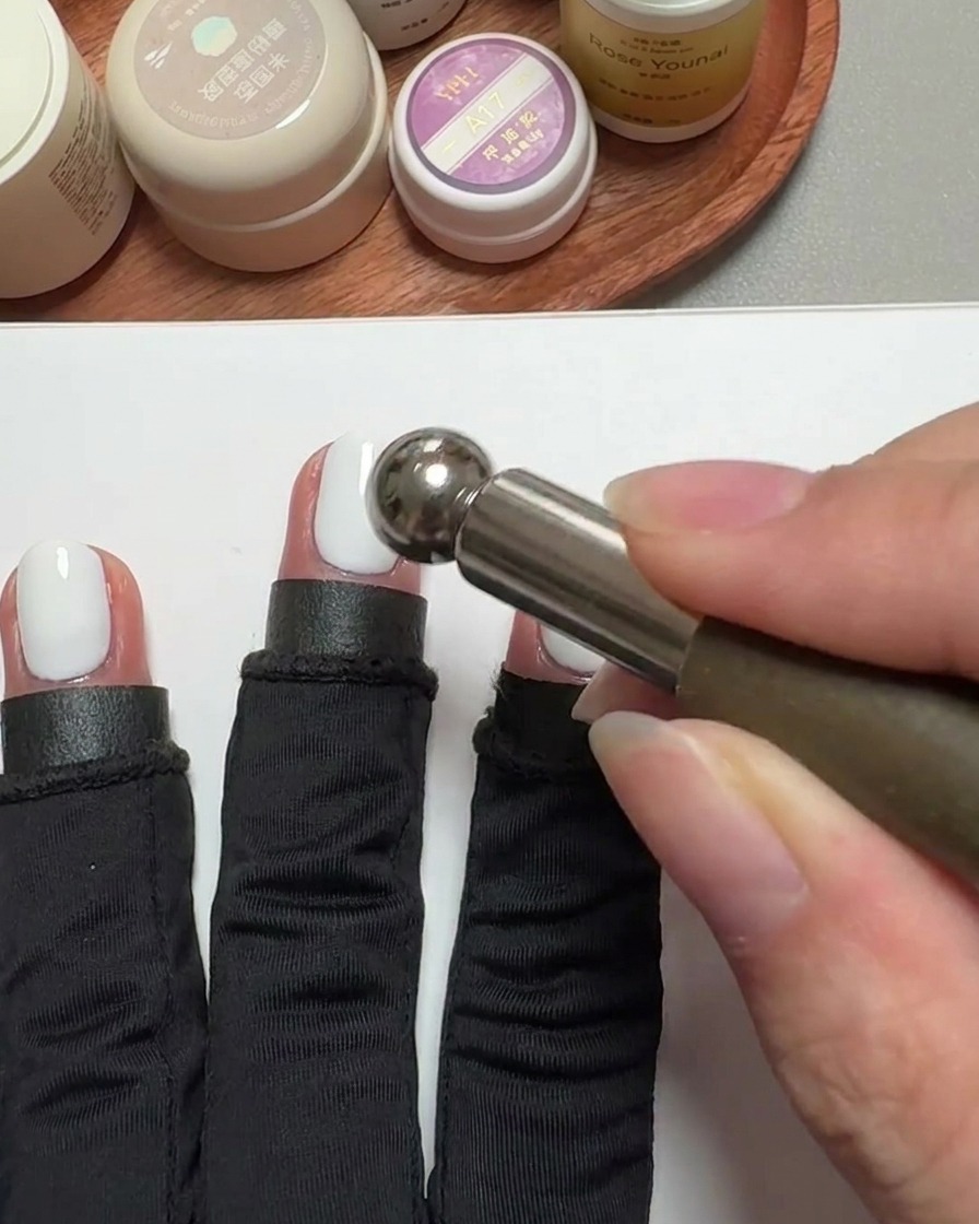 Primer plano de una herramienta magnética cilíndrica sobre una uña con gel para crear el efecto cat-eye.