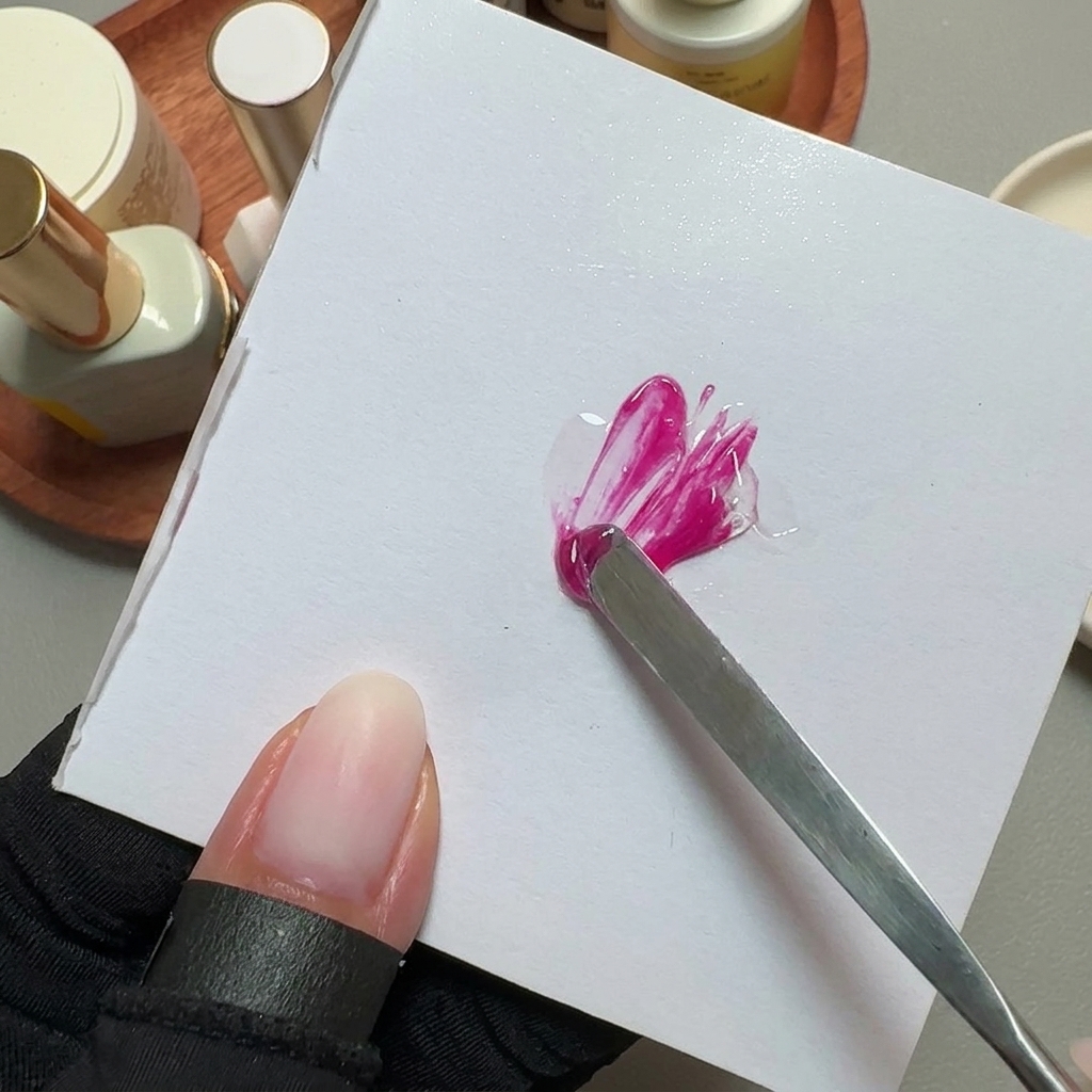 Una espátula de metal mezclando esmalte de gel rosa brillante en una paleta cuadrada blanca.