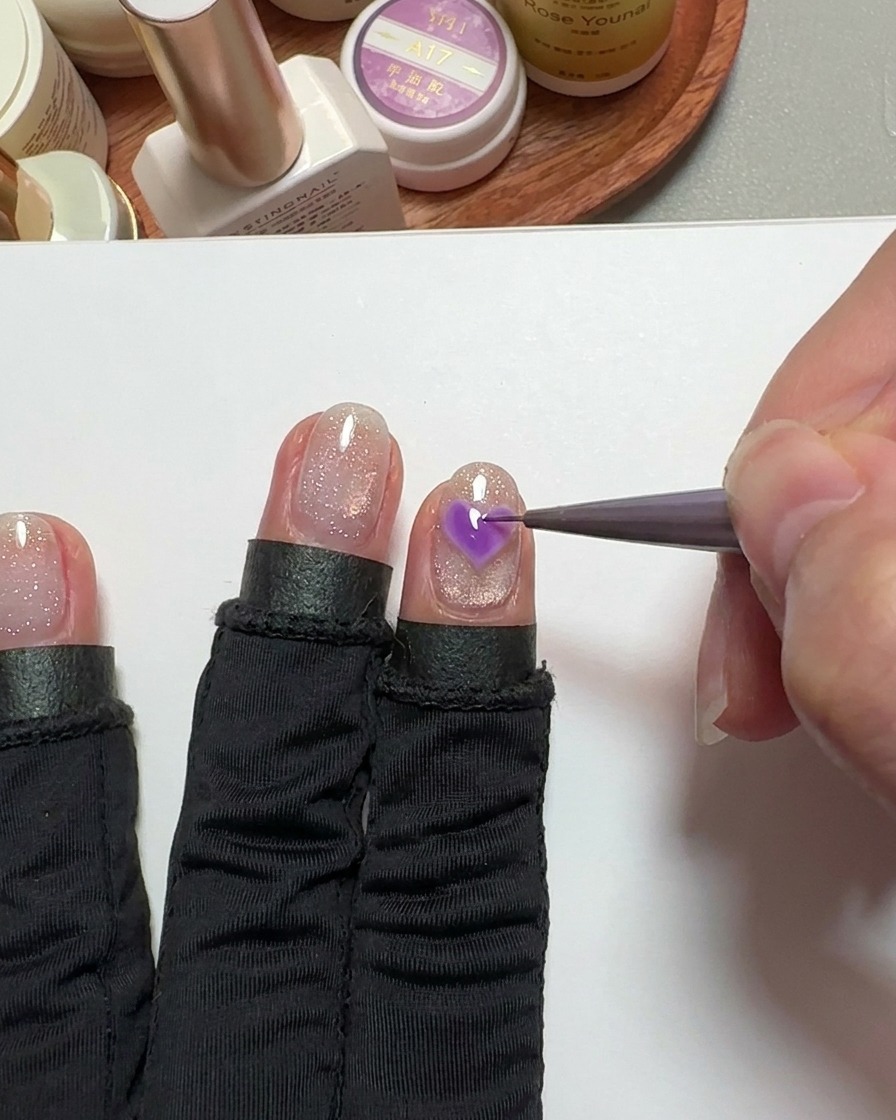 Un pincel de detalle fino rellenando un corazón en la uña con gel rosa.