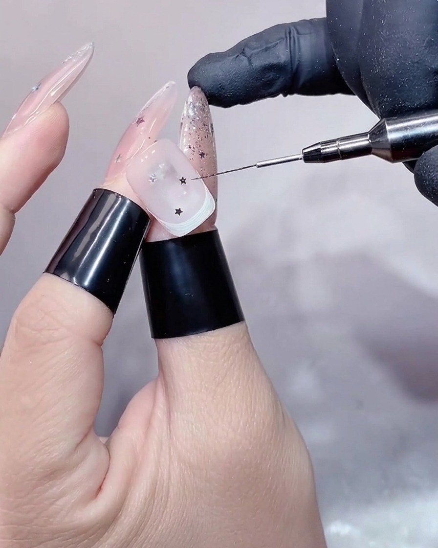 Primer plano de una mano dentro de una lámpara UV/LED, enfocando la uña decorada con estrellas plateadas durante el proceso de secado.