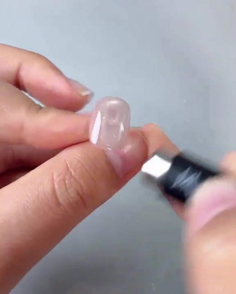 Una mano sosteniendo un imán cilíndrico sobre una uña rosa, creando un reflejo circular brillante.