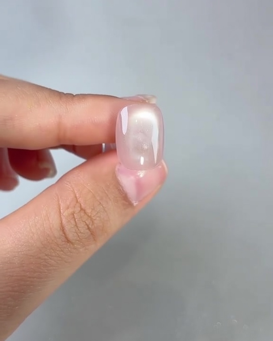 Un pincel aplicando top coat transparente sobre una uña de gel cat-eye curada.