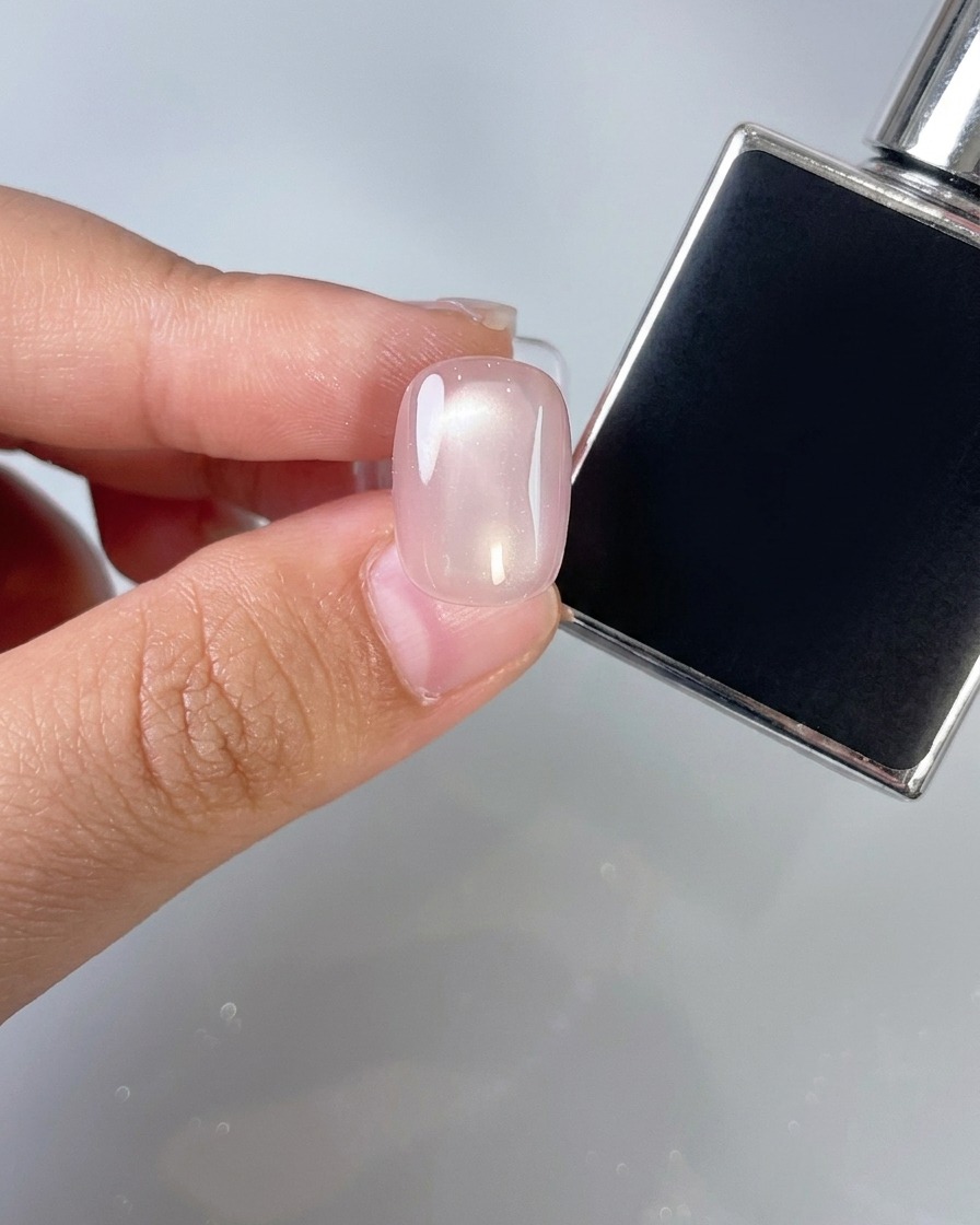 Un pincel aplicando una capa de top coat transparente sobre una uña rosa.