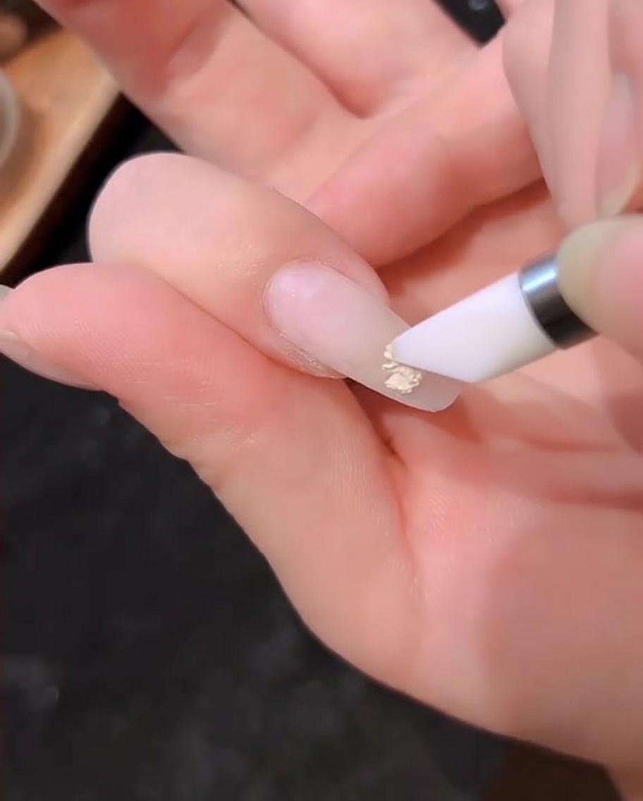 Un pincel de esmalte aplicando una capa de gel color blanco lechoso sobre la uña.