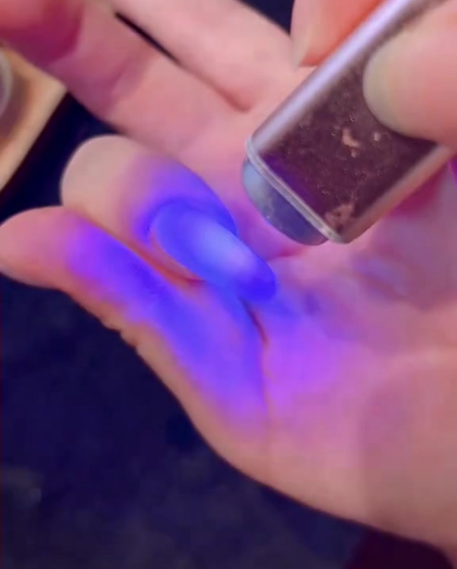 Un pincel aplicando una capa de gel con brillos tipo diamante sobre la uña.