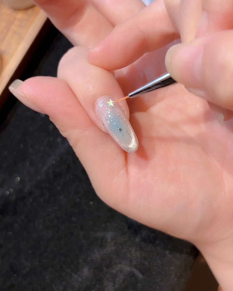 Un pincel fino colocando una estrella holográfica sobre el gel húmedo.