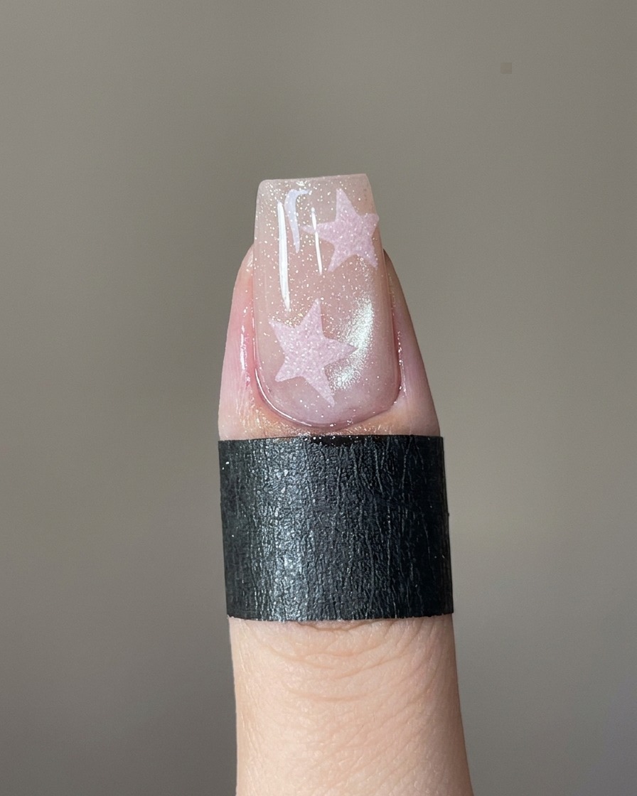 Un pincel de detalle fino rellenando una plantilla de estrella en una uña con gel rosa.