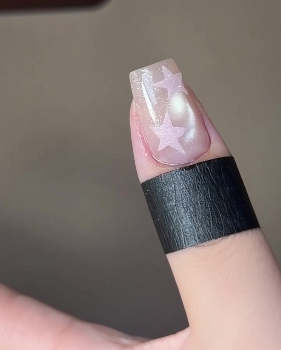Dedos curando un diseño de uñas con estrella bajo una lámpara UV profesional.