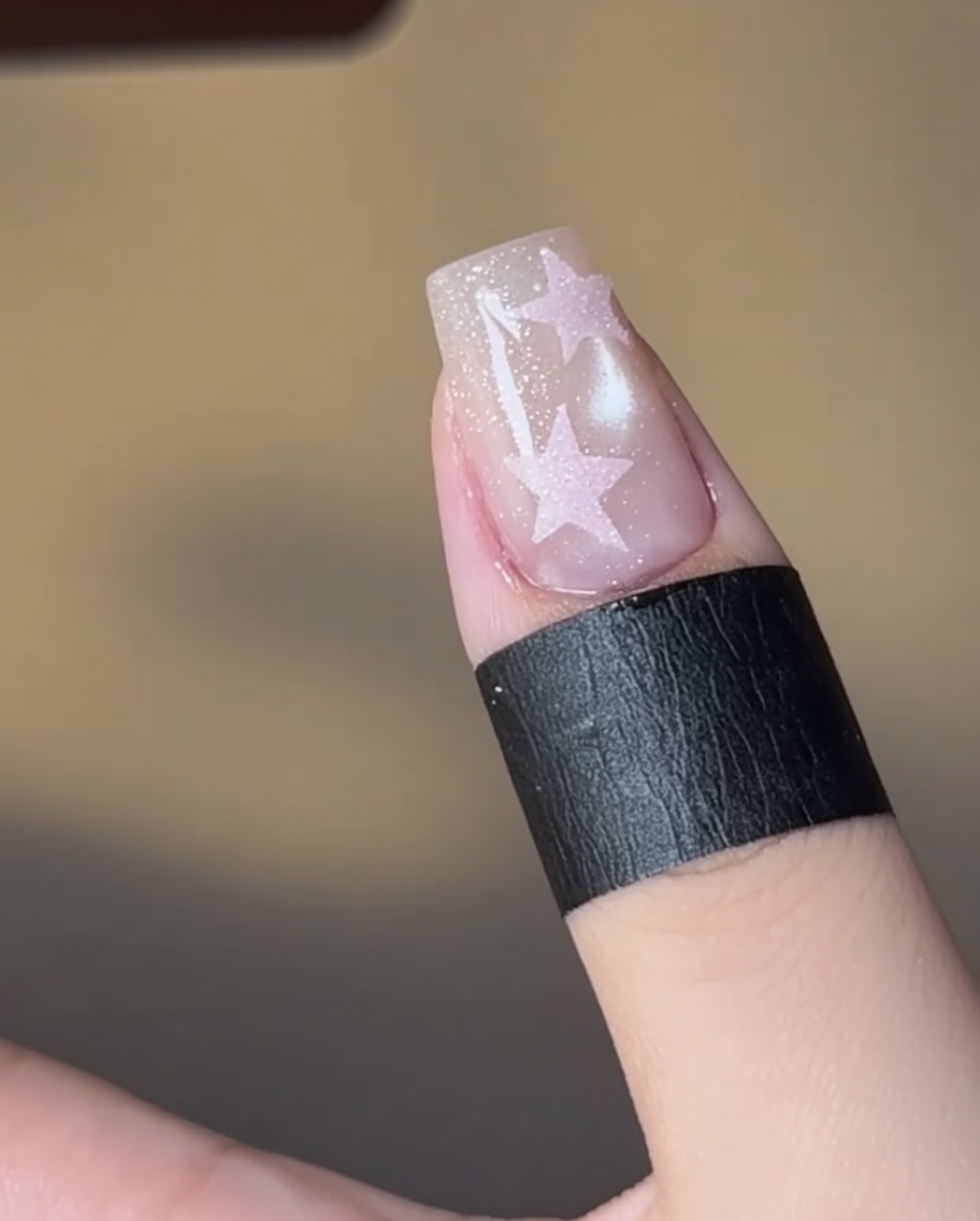 Una uña con un diseño de estrella relleno de rosa curándose bajo una lámpara.