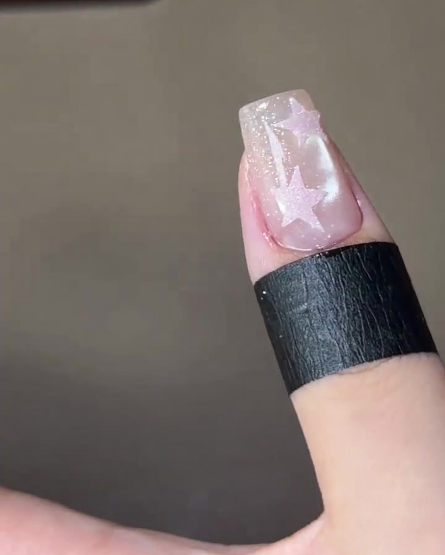 Primer plano de un pincel aplicando un top coat brillante y transparente sobre una estrella rosa pintada en una uña reluciente.
