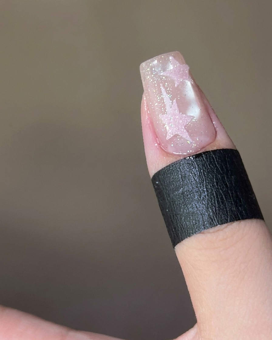 Polvo de azúcar rosa siendo espolvoreado sobre una estrella cubierta de top coat húmedo en una uña.