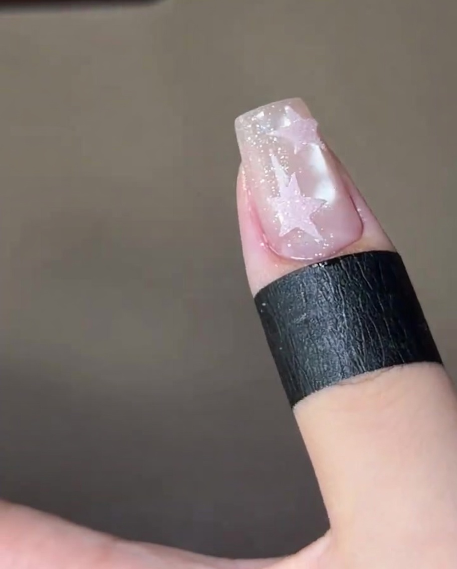 Una uña terminada con dos estrellas de azúcar rosas texturizadas, curándose dentro de una lámpara de uñas UV.