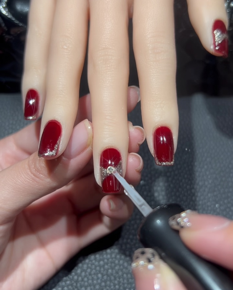 Una gota de pegamento transparente para uñas siendo colocada en el centro del diseño del lazo de glitter.