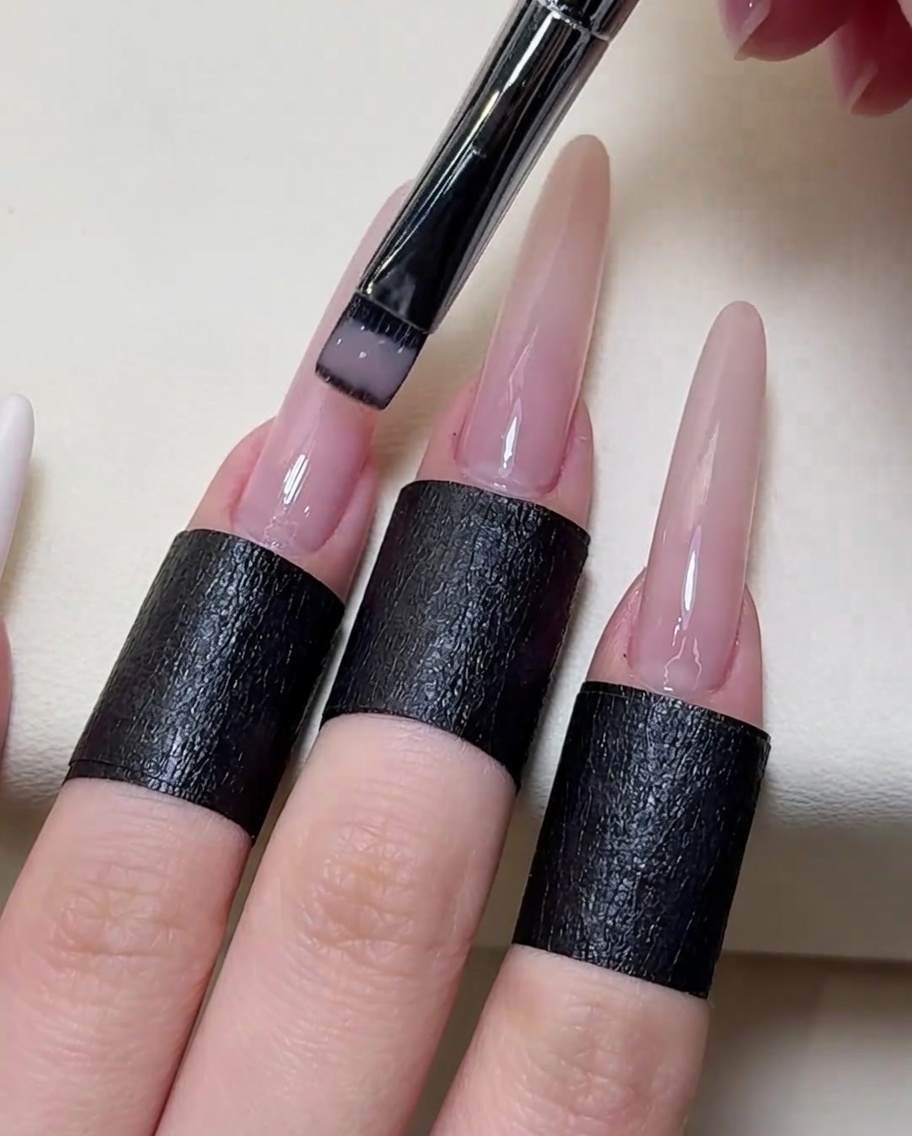 Primer plano de un pincel aplicando esmalte de gel nude transparente sobre la uña.
