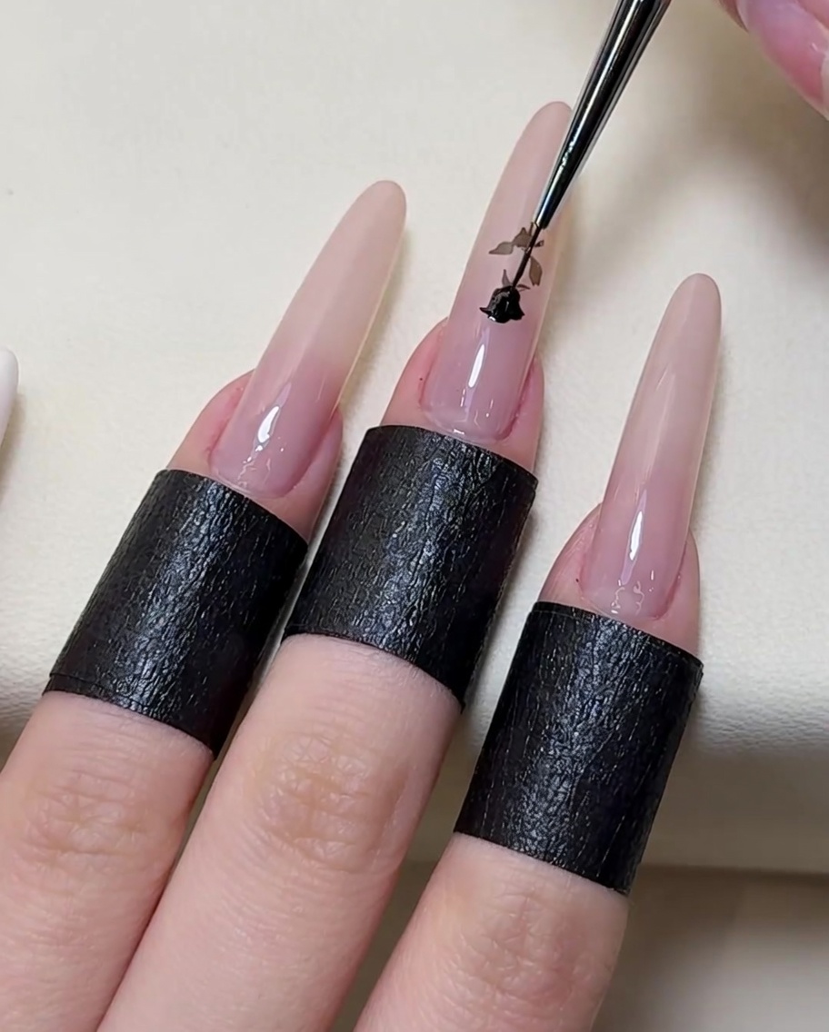 Un pincel de detalle fino repasando y rellenando los detalles del diseño de la rosa con gel negro.
