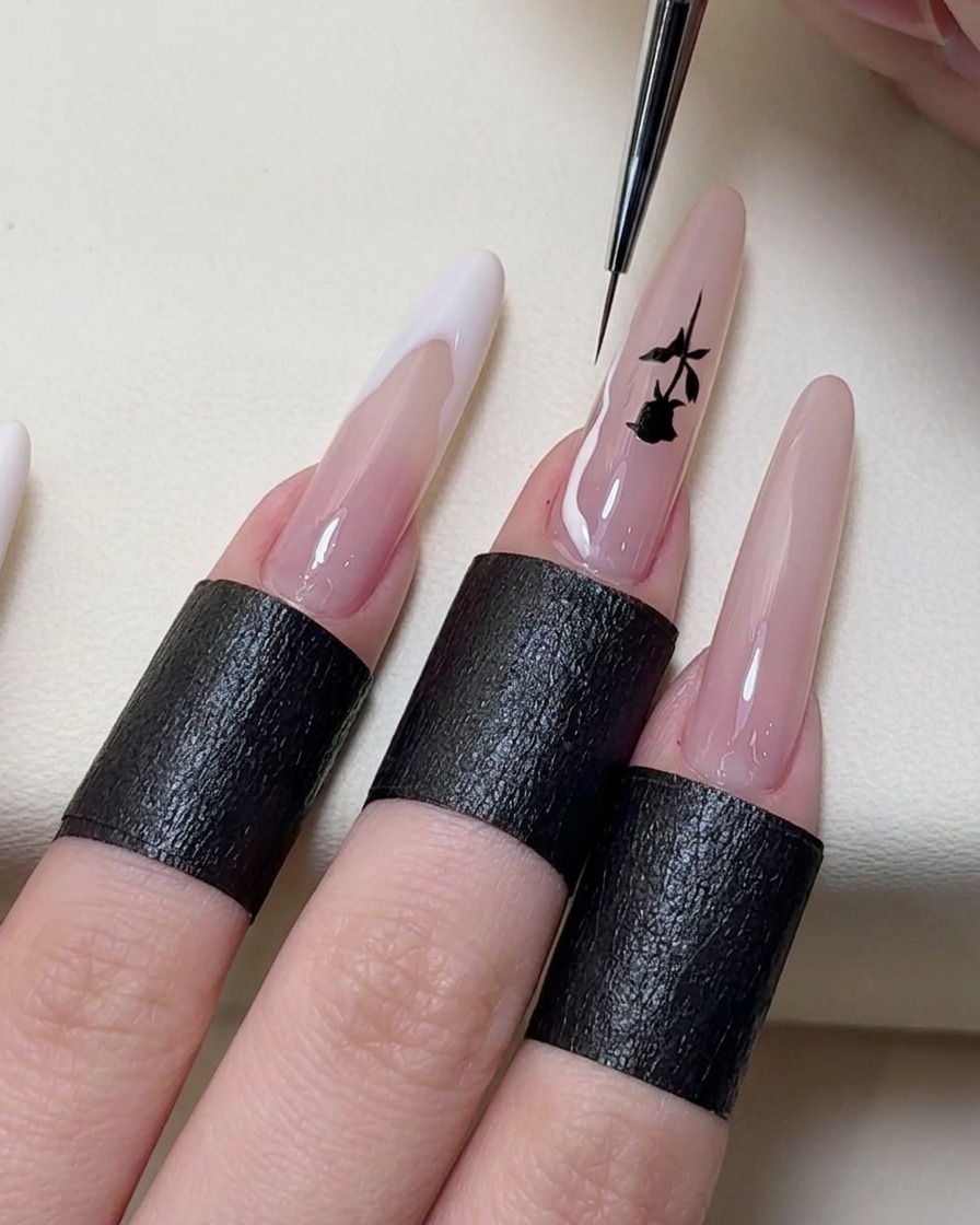 Un pincel de nail art pintando líneas de punta francesa irregulares en blanco en los extremos de las uñas.