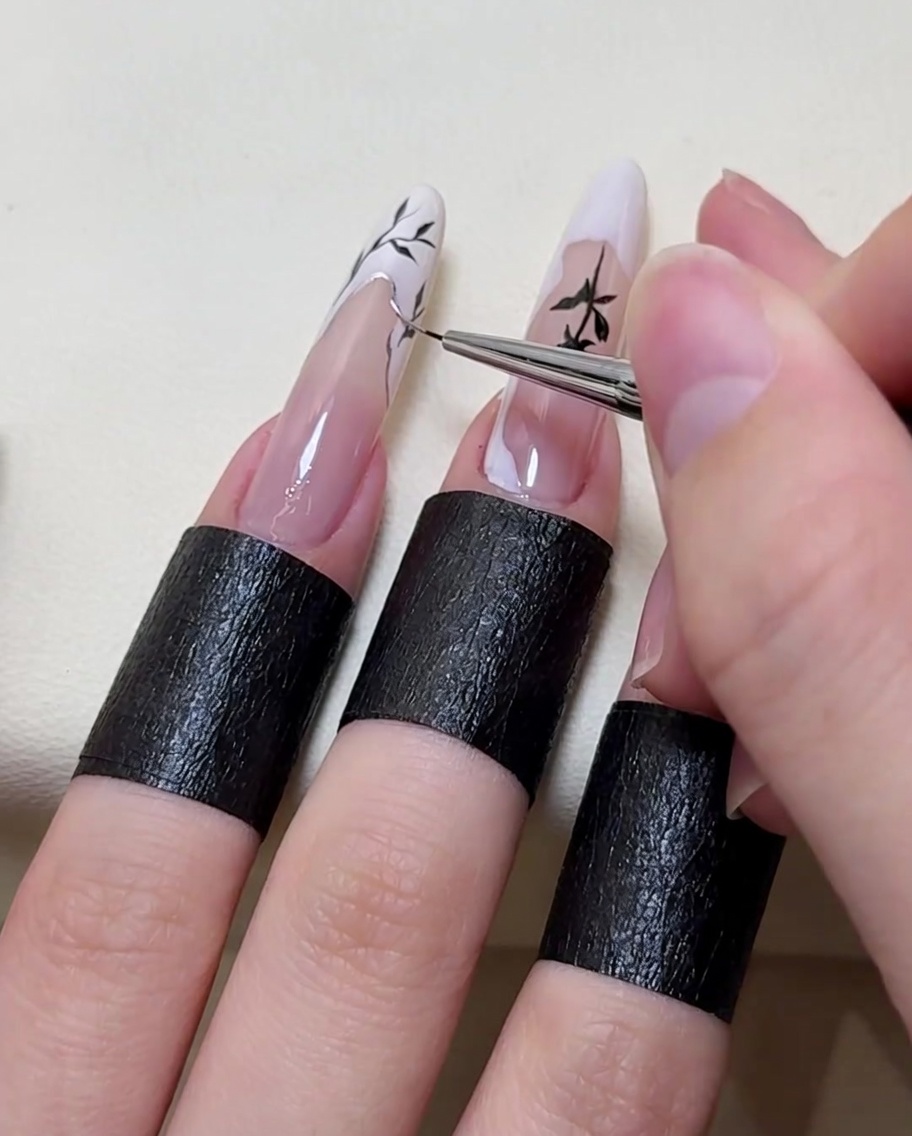 Un pincel de nail art aplicando un reflejo plateado metálico a lo largo del borde del diseño de la rama.