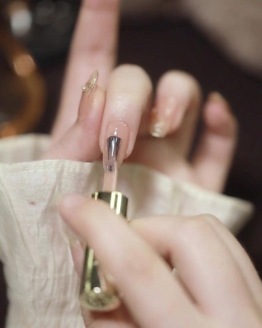 Primer plano de un pincel de uñas aplicando esmalte gel nude sobre una uña limpia y preparada.