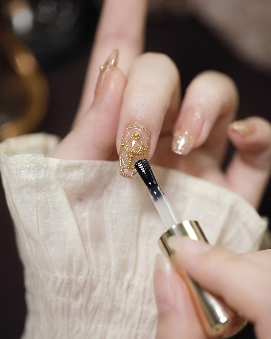 Un pincel de gel transparente aplicando una capa protectora sobre una uña decorada con cromo y perlas.