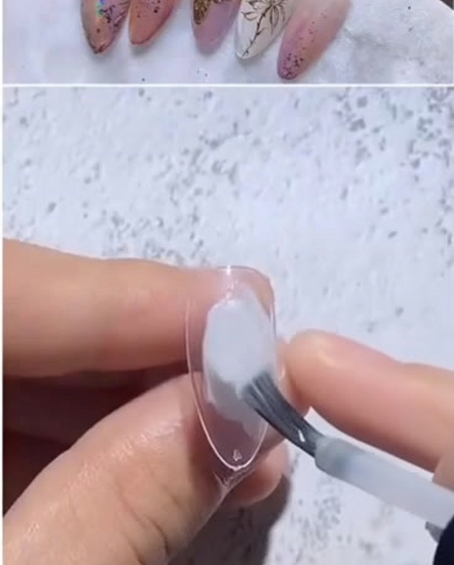 Primer plano de un tip almendrado recibiendo una gota de esmalte de gel blanco lechoso con un pincel.