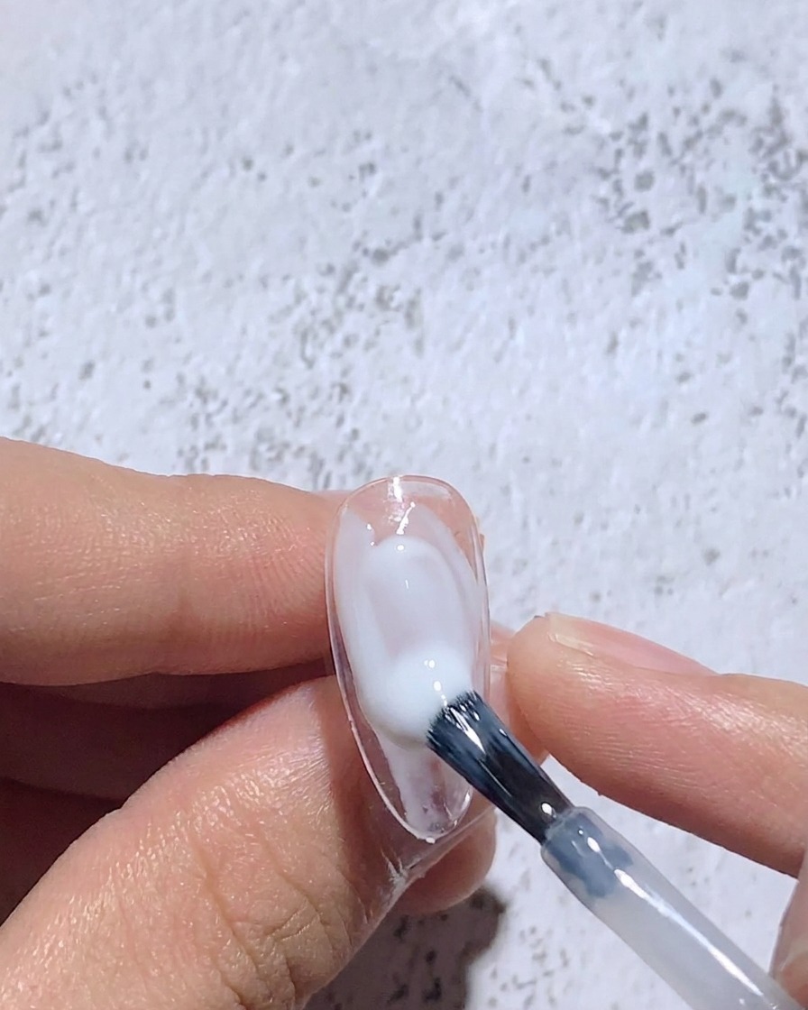 Un pincel fino difuminando gel blanco húmedo sobre un tip para crear un centro suave.