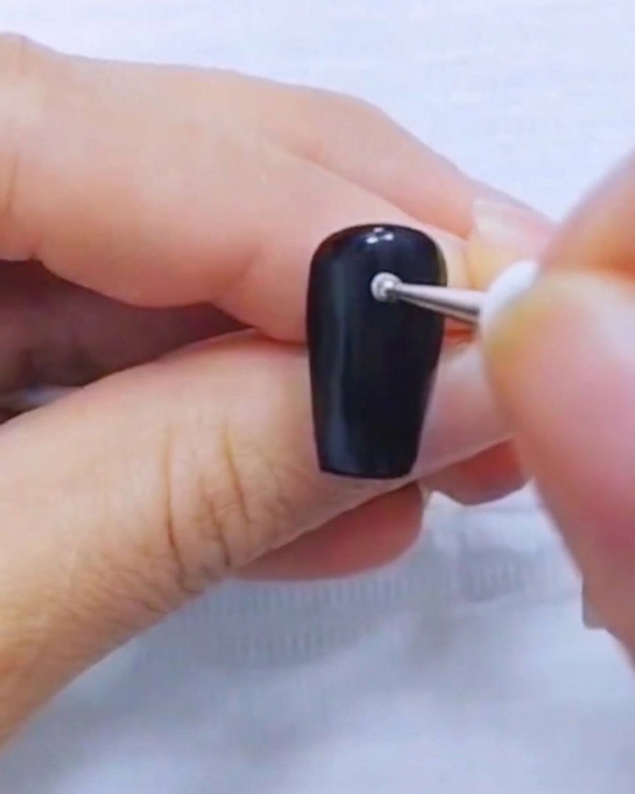 Primer plano de un punzón colocando un pequeño punto blanco en una uña negra sólida.