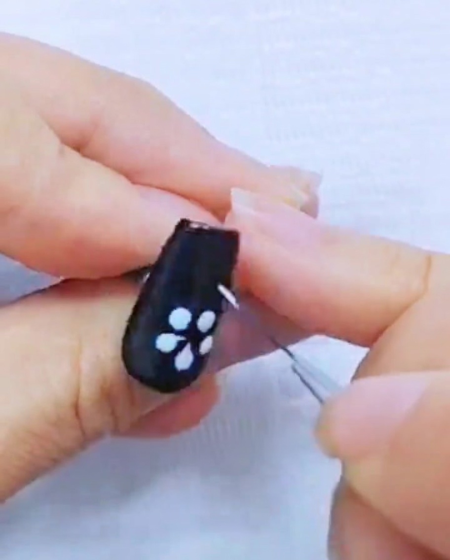 Primer plano de un pincel liner refinando los pétalos de gel blanco sobre una uña negra.