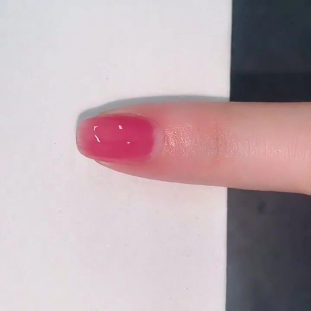 Una sola uña cubierta con una capa translúcida y brillante de esmalte jelly rosa.