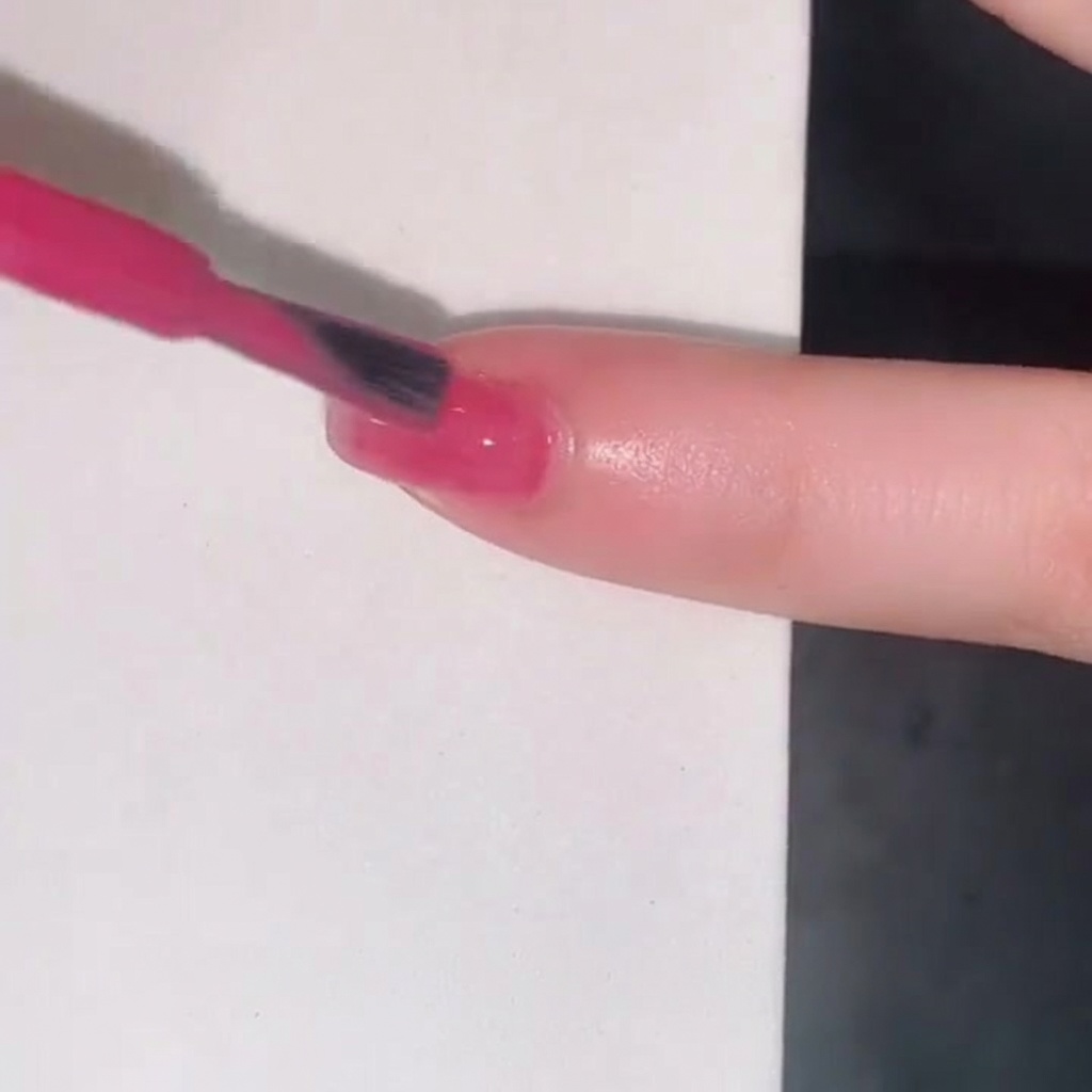 Un pincel de esmalte añadiendo una tercera capa de gel jelly rosa para intensificar el color en la uña.