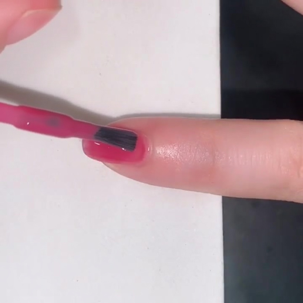 Un pincel aplicando un esmalte jelly rosa translúcido sobre una uña.