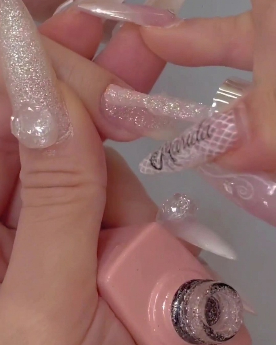 La punta de un pincel de esmalte aplicando un top coat transparente y brillante sobre una uña texturizada con glitter.