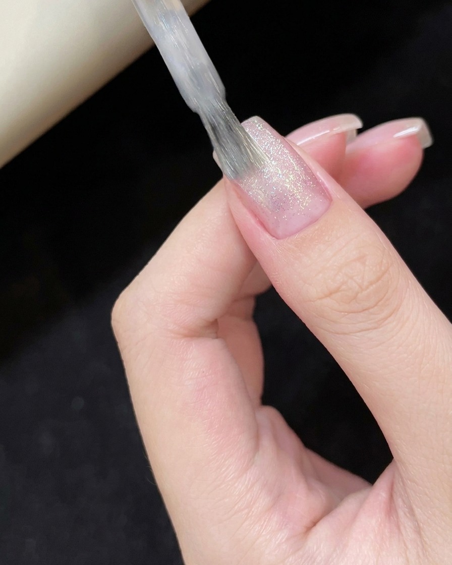 Aplicando esmalte cat-eye blanco traslúcido sobre la superficie de la uña.