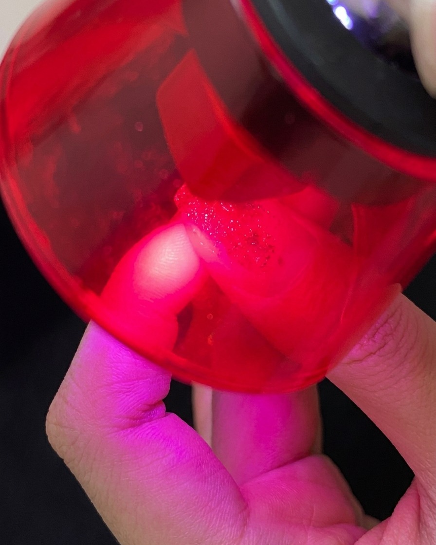 Un pincel aplicando una capa superior transparente y brillante sobre una uña decorada con gel cat-eye azul, líneas blancas y estrellas plateadas.
