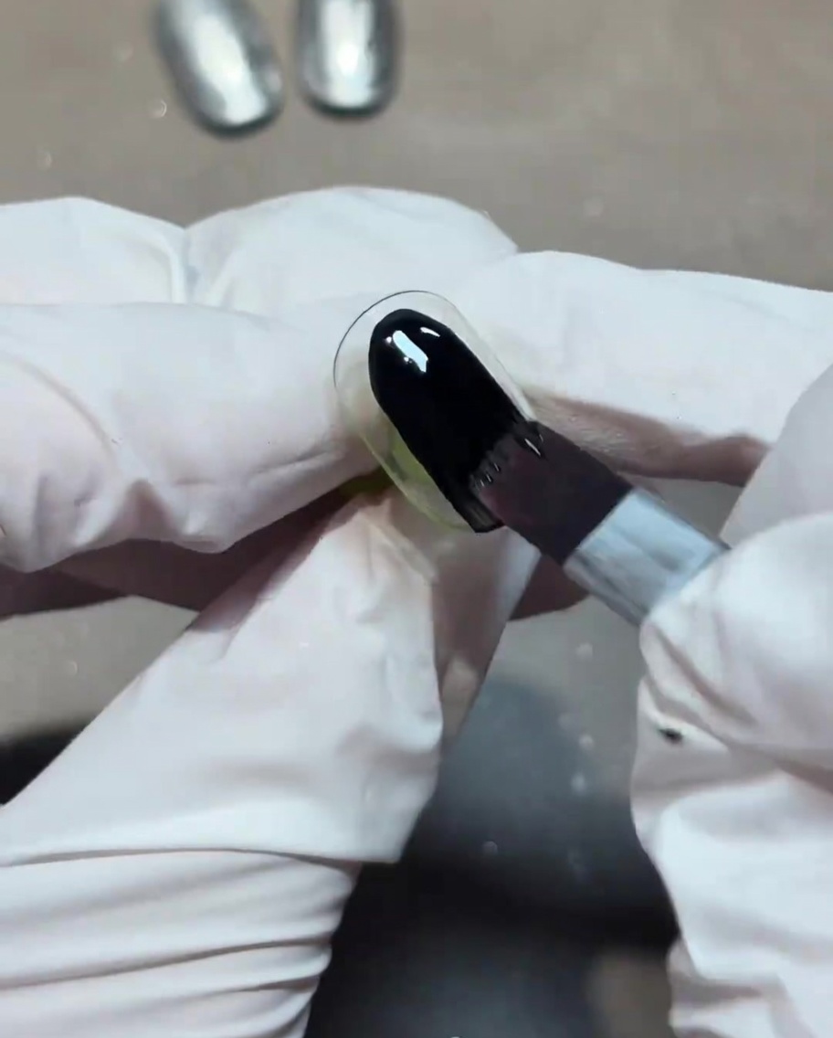 Un pincel aplicando una capa de esmalte de gel negro opaco sobre una uña.