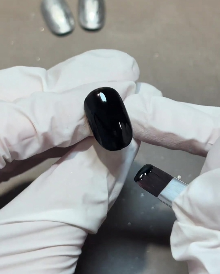Aplicando un top coat transparente y brillante sobre una base de uña negra.