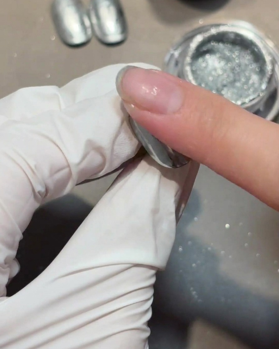 Aplicando una capa de gel de refuerzo transparente sobre una uña con cromo.
