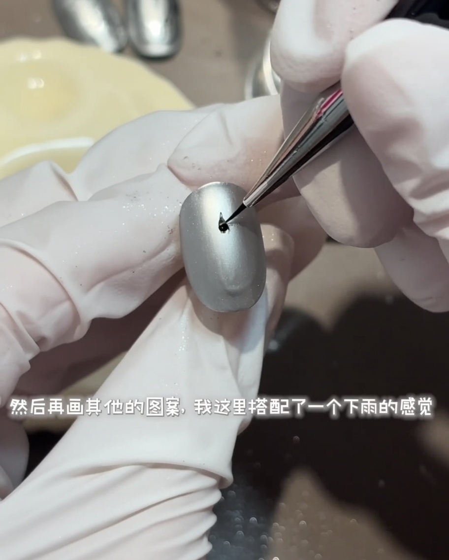 Un pincel fino dibujando un diseño detallado de ondas de agua circulares con top coat brillante sobre una uña gris mate.