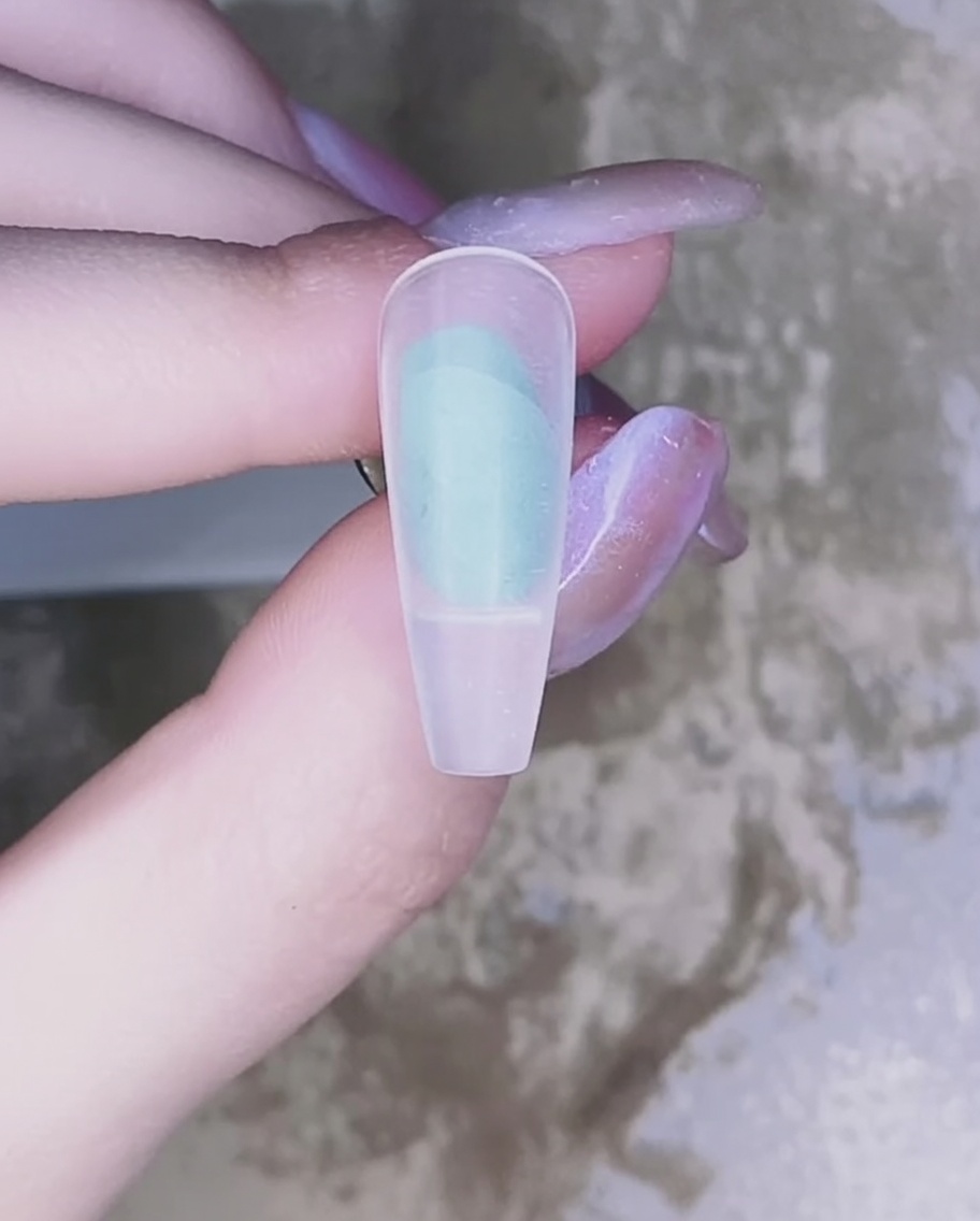 Primer plano de un pincel aplicando esmalte de gel rosa translúcido sobre la superficie de una uña natural.