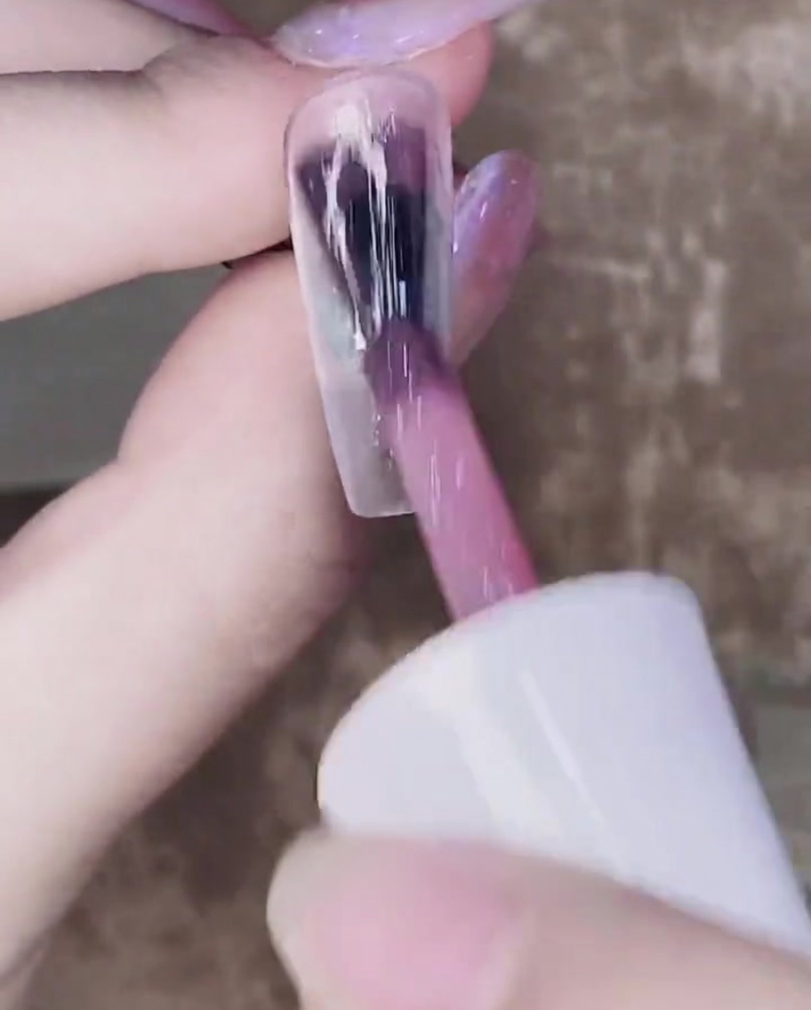 Un pincel aplicando una segunda capa de gel rosa translúcido sobre la primera capa ya curada.