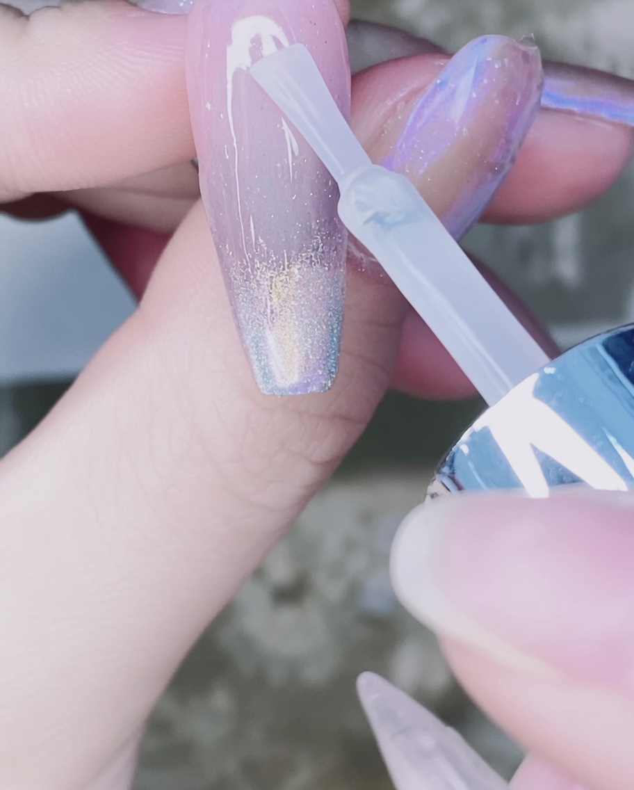 Un pincel de uñas aplicando top coat transparente sobre el degradado de polvo cromado en la uña.