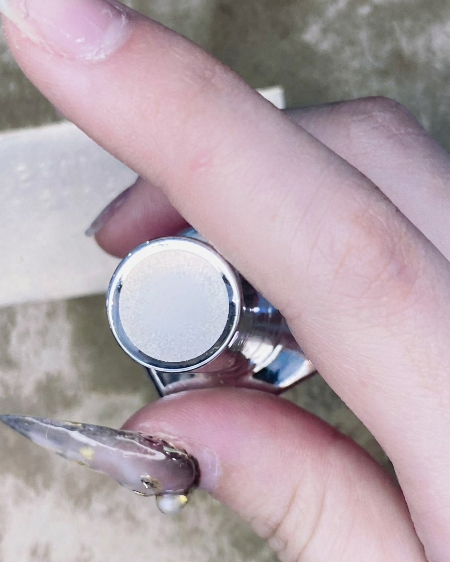 Un pincel fino para arte de uñas aplicando una pequeña gota de top coat alrededor de la base de una pedrería montada en una uña.