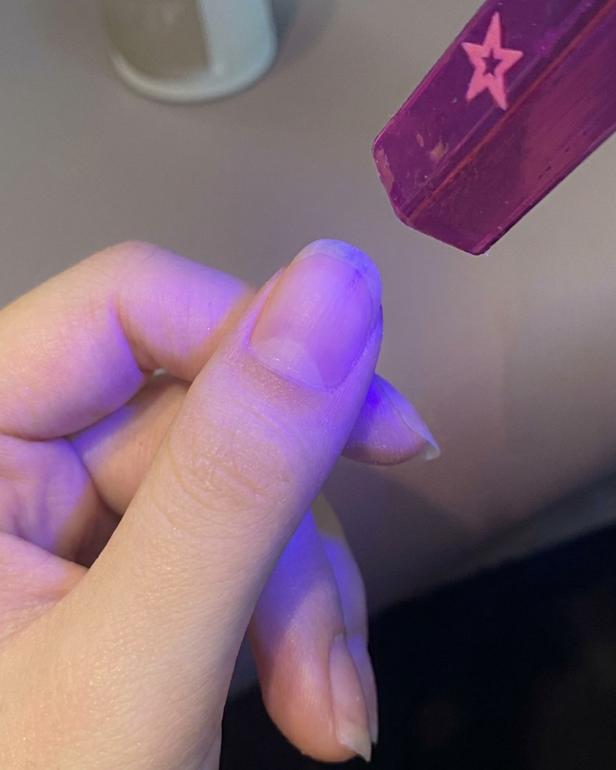 Una mano colocando una uña bajo una pequeña lámpara UV portátil para curar la base.
