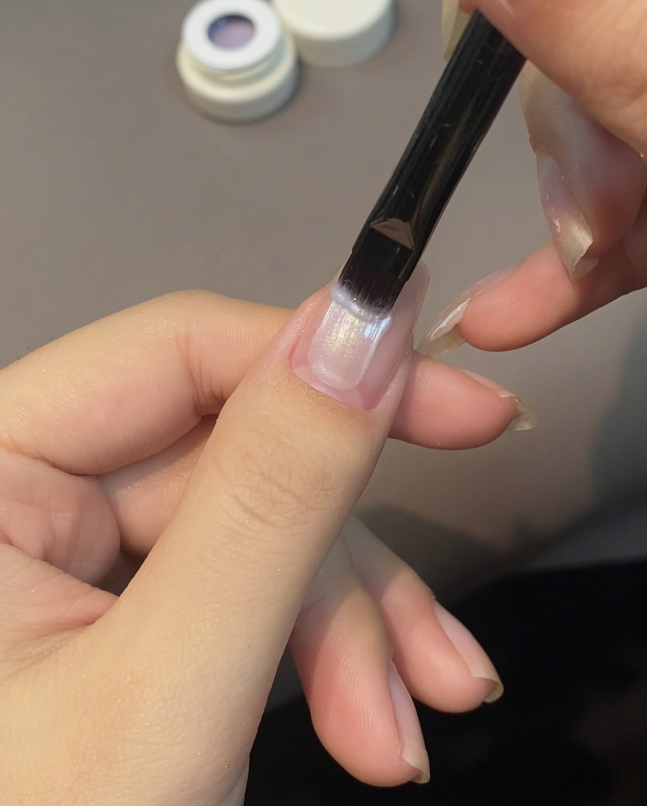 Un pincel aplicando gel ojo de gato morado claro sobre la superficie de una uña.
