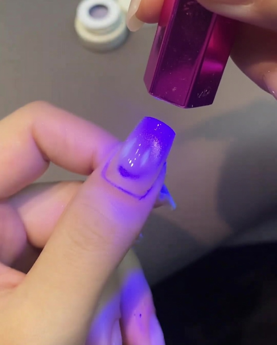Una uña con gel ojo de gato siendo curada bajo una mini lámpara UV.