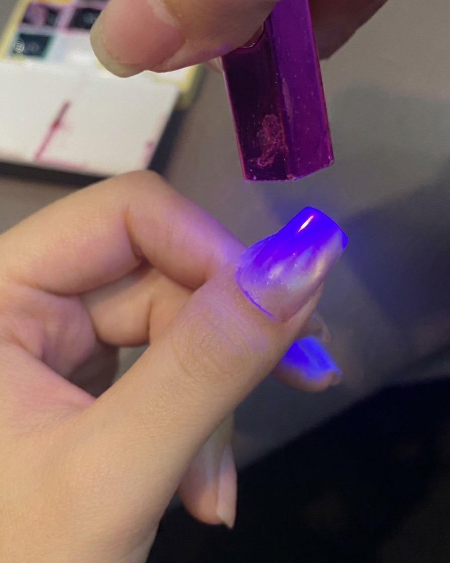 Una uña siendo curada bajo una mini luz UV.