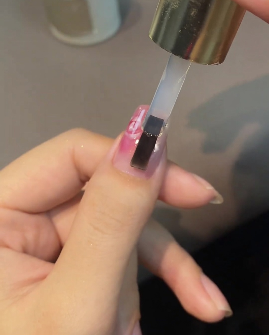 Un pincel aplicando top coat transparente sobre un diseño de rosa pintada.